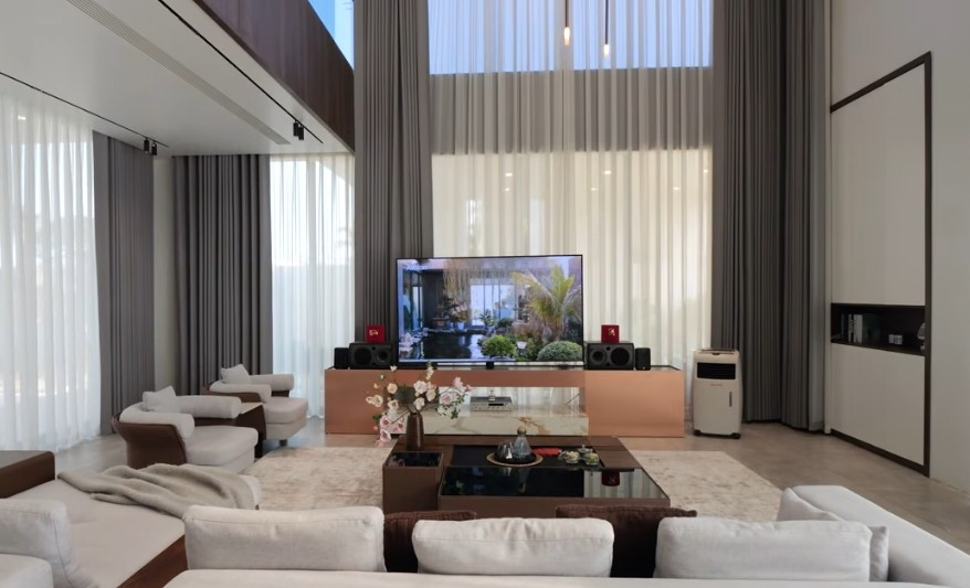 Phòng khách sử dụng nhiều cửa kính lớn lấy ánh sáng và bao quát không gian bên ngoài. Ảnh chụp màn hình