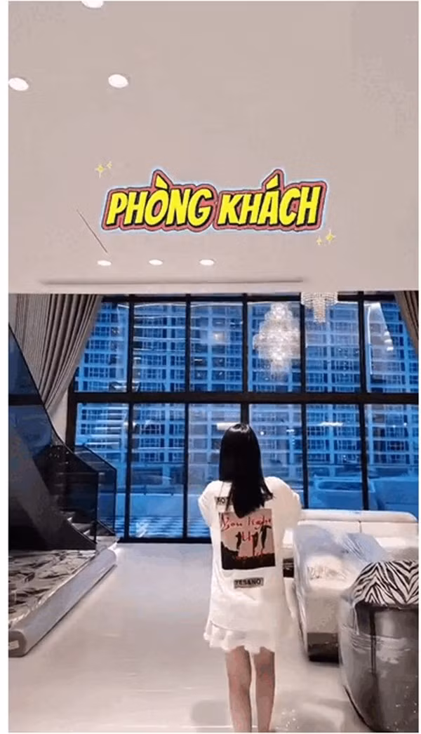 Phòng khách thông tầng rộng rãi, đón ánh sáng tự nhiên tràn ngập qua hệ cửa kính lớn hướng ra bên ngoài. Ảnh chụp màn hình