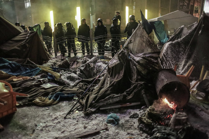 Lực lượng Berkut đứng phía ngoài hàng rào chắn nhìn về phía lều trại bị cháy rụi của người biểu tình.
