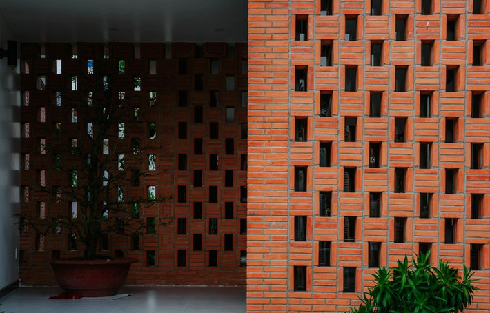 gôi nhà sử dụng chủ yếu bằng vật liệu gạch thô. Nhóm thiết kế 90odesign sử dụng phương án tận dụng hình thức đặc biệt của mặt bằng, chủ động đặt các khu chức năng xoay quanh khu vườn giữa nhà. Mặt tiền được tách thành hai lớp gạch đất nung, xen kẽ cửa chính và sảnh đệm. Giải pháp này giúp giảm nắng chiếu trực tiếp vào mặt nhà và tạo điều kiện thông gió tự nhiên vào sâu bên trong, cũng như có sự kín đáo cần thiết cho gia chủ.