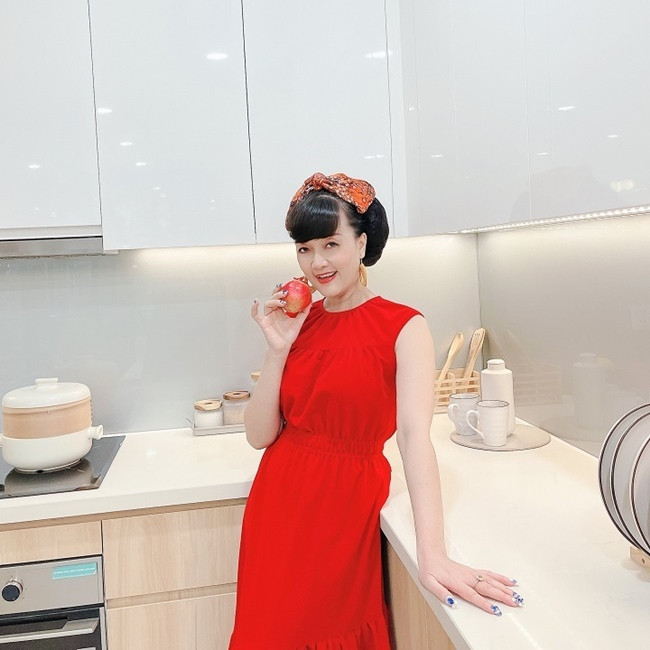 Vân Dung chọn băng đô hoa và bông tai màu vàng nâu để kết hợp váy liền đỏ ngắn tay và chi tiết hạ eo giúp người mặc thêm thon gọn.
