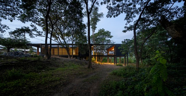 Ngôi nhà nằm ở ven đường của cánh rừng dương xỉ tươi xanh tại quận Chom Thong, Chiang Mai, Thái Lan. Để tôn trọng thiên nhiên hiện có, ngôi nhà được thiết kế theo chiều dài của khu đất và ôm trọn các cây xanh.