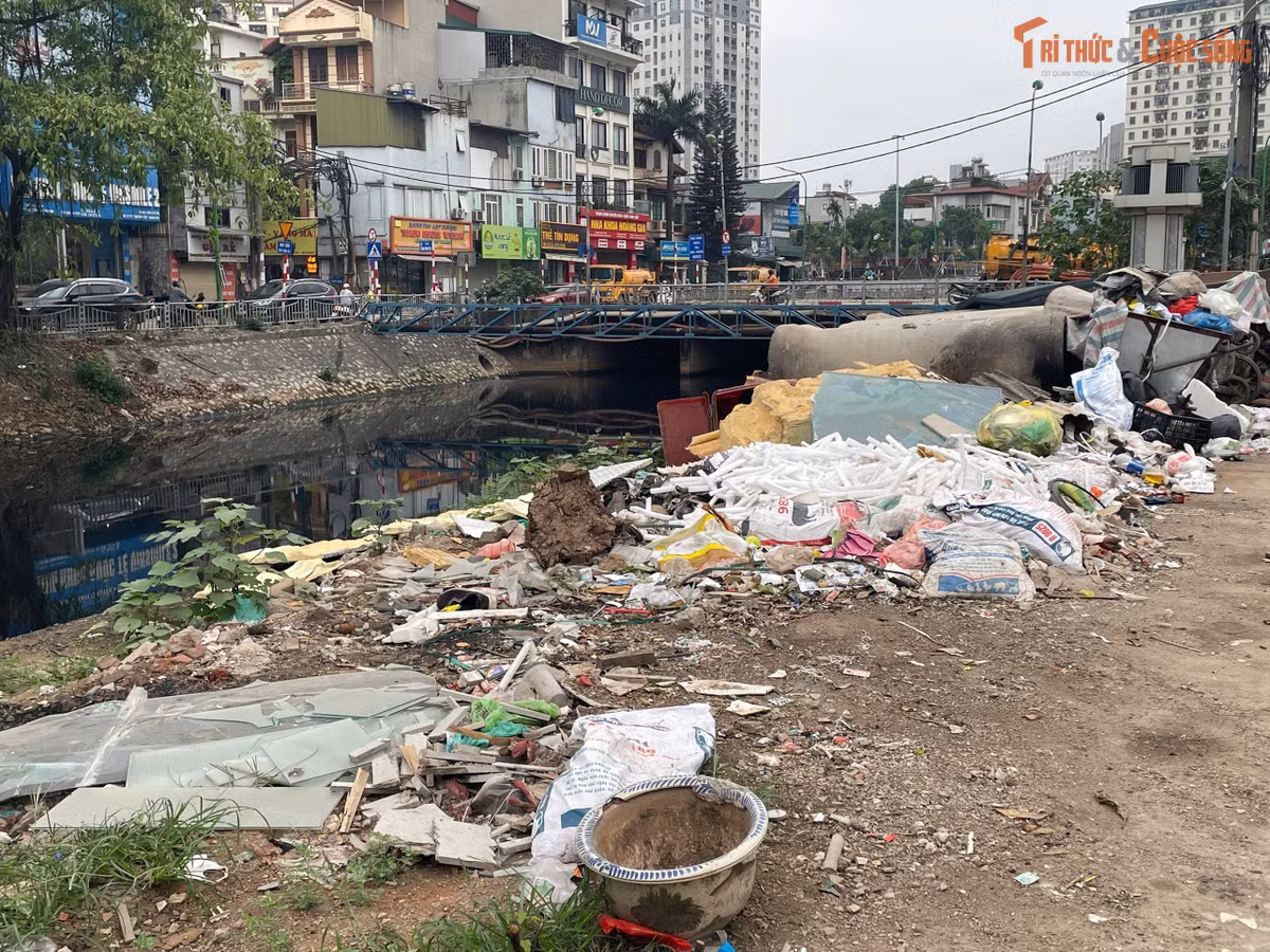 Một bãi rác tự phát nằm ngay sát lòng đường, phía sau là đất đổ và vật liệu xây dựng chưa được xử lý. Những bao tải, nệm cũ, nhựa và gạch đá chất thành từng lớp, xe chở vật liệu xếp thành hàng dài càng cho thấy sự lộn xộn trong quá trình thi công dở dang.