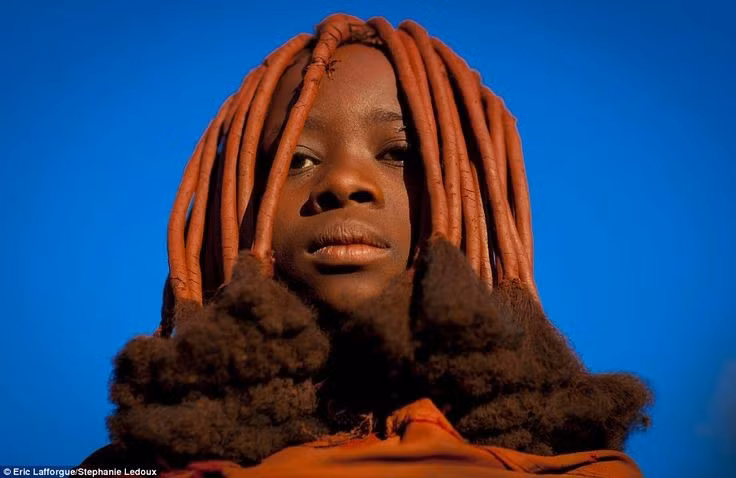  Nổi tiếng với lớp bôi da màu đỏ. Cư dân Himba thường trộn mỡ bò với bột đá ochre đỏ để bôi lên da và tóc. Hỗn hợp này giúp bảo vệ da khỏi nắng gắt, côn trùng và đồng thời mang ý nghĩa thẩm mỹ, tâm linh sâu sắc. Ảnh: Pinterest.