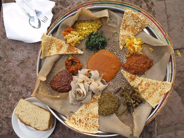  Văn hóa ẩm thực độc đáo. Ẩm thực Amhara nổi bật với bánh injera làm từ ngũ cốc teff và các món hầm cay gọi là wot, thể hiện lối ăn uống cộng đồng và truyền thống hiếu khách lâu đời. Ảnh: Pinterest.