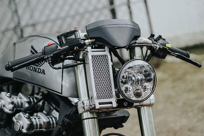 Về thiết kế của chiếc Honda CB750 độ cafe racer này, thay vì kiểu dáng đầu đèn tròn cổ điển, xưởng độ đã khiến chiếc xe cá tính hơn với phần đầu là một đèn LED dạng thấu kính projector hiện đại, bên cạnh đó là két tản nhiệt dầu được thiết kế đẩy hẳn lên cao sát với tay lái của chiếc xe.