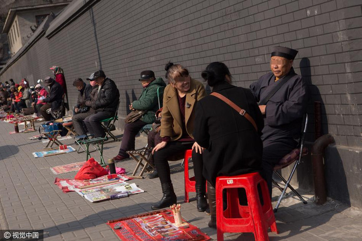 Trong ảnh là một thầy bói khăn áo đầy đủ đang xem bói cho khách hàng. Trong khi đó các quầy xem bói, xem tướng số khác chưa có khách. (Nguồn Sina)