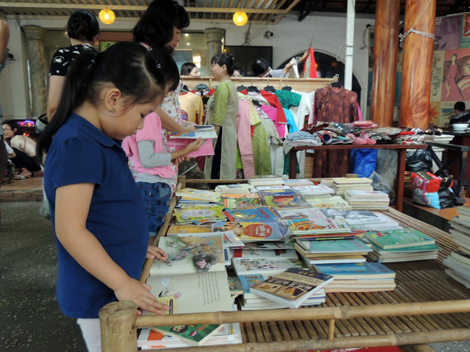 Một bạn nhỏ tranh thủ đọc sách khi vắng khách. 10-15% lợi nhuận từ phiên chợ sẽ được các tiểu thương “nhí” cùng bố mẹ chia sẻ cho những dự án thiện nguyện ý nghĩa.