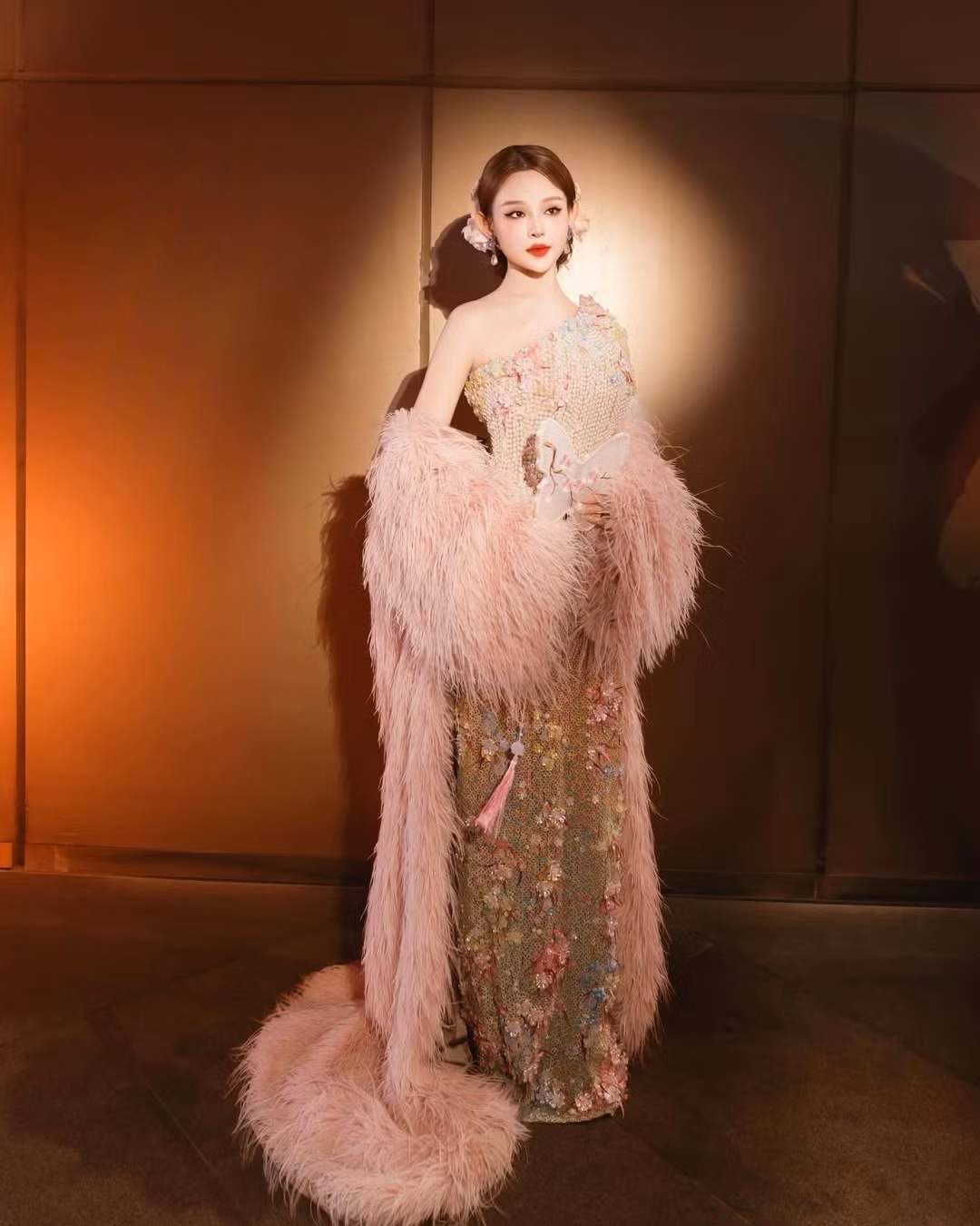 Điểm nhấn đắt giá nhất chính là chiếc khăn choàng lông vũ màu hồng pastel khổng lồ. Chiếc khăn không chỉ tạo độ bồng bềnh, quyền lực mà còn kéo dài thành đuôi váy quét đất, giúp mỗi bước đi của "chị đẹp" trên thảm đỏ trở nên uyển chuyển và thu hút hơn bao giờ hết. (Ảnh: IGNV)
