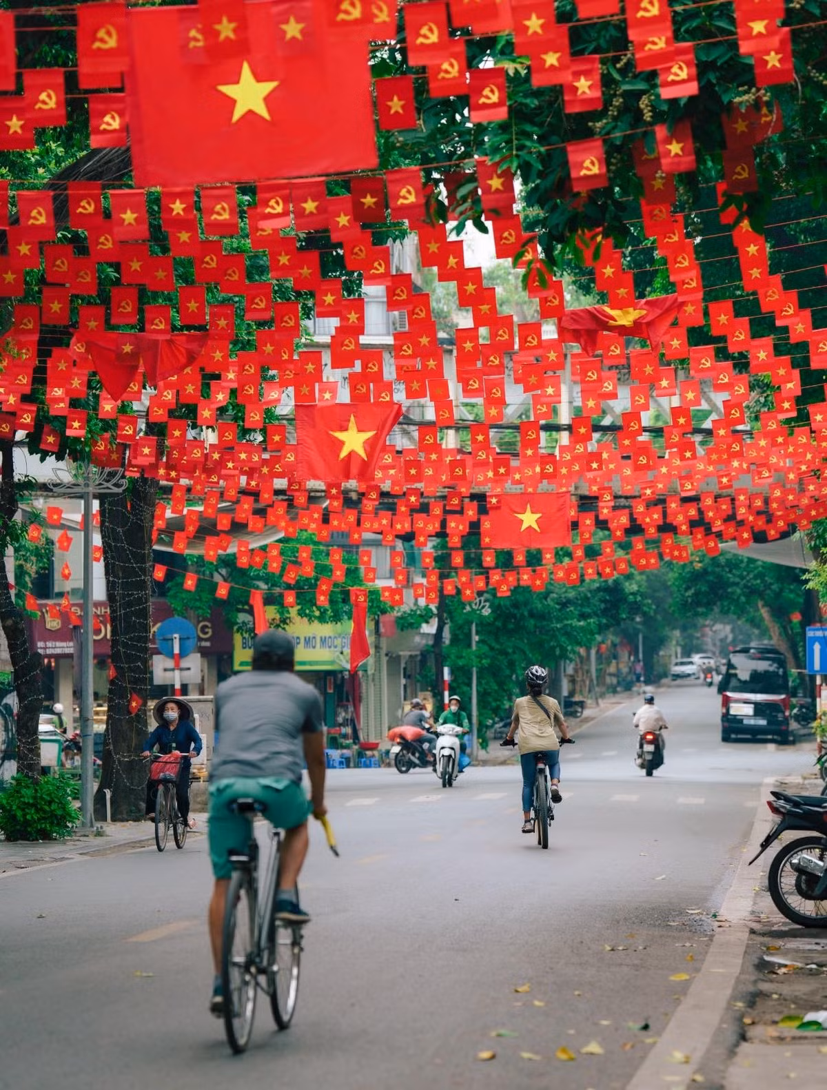 Trong không gian tràn ngập màu cờ, cuộc sống thường nhật của người dân Thủ đô vẫn diễn ra nhịp nhàng. Những người đi xe đạp, xe máy, hay những gánh hàng rong vẫn lặng lẽ di chuyển dưới những dải cờ. (Ảnh: Blog Của Rọt)