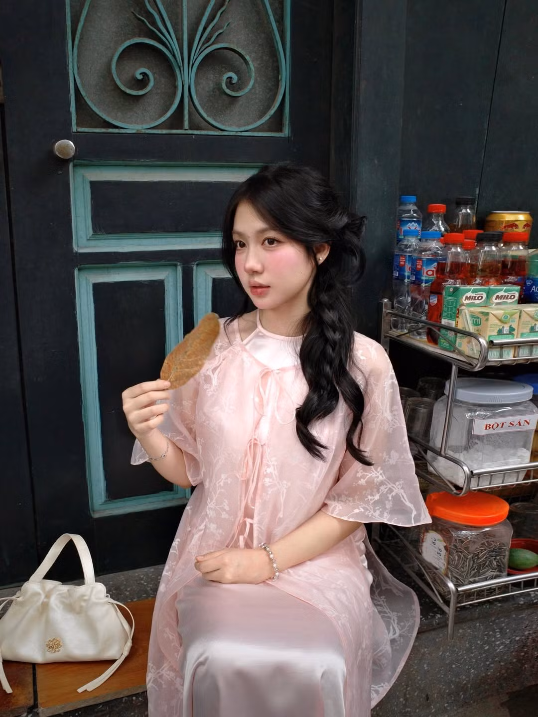Trong bộ ảnh, cô gái diện chiếc áo dài cách tân với thiết kế tinh tế, lớp ngoài là chất liệu voan mỏng manh màu hồng pastel, điểm xuyết họa tiết hoa nhí hoặc cành cây trắng thanh lịch, kết hợp cùng lớp lót lụa mềm mại bên trong. (Ảnh: IGNV)