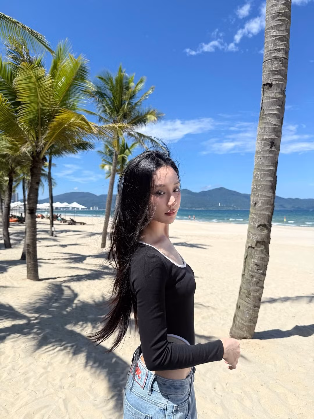 Loạt ảnh mới nhất cho thấy Mina Young đang tận hưởng kỳ nghỉ tại bãi biển thơ mộng, với bối cảnh là bãi cát trắng mịn, hàng dừa xanh mát và núi non hùng vĩ phía xa. (Ảnh: IGNV)