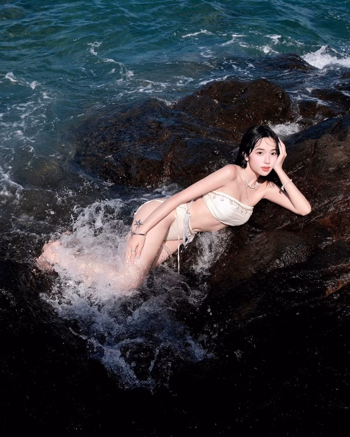 Màu sắc nude pastel không chỉ tôn lên làn da trắng mịn màng mà còn tạo nên sự hòa quyện hoàn hảo với khung cảnh biển xanh và đá đen tự nhiên. (Ảnh: FBNV)
