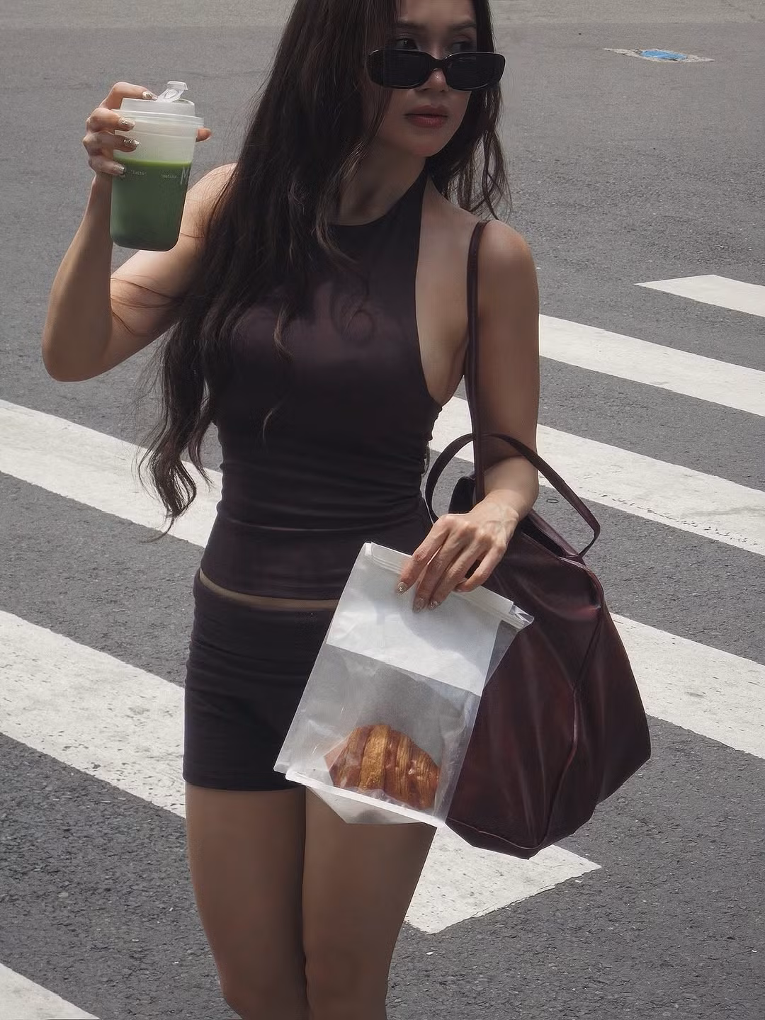 Sĩ Thanh xuất hiện với mái tóc dài bồng bềnh, gương mặt trang điểm sắc sảo, tự tin cầm trên tay ly nước và một chiếc bánh croissant, tạo nên những khoảnh khắc đời thường nhưng vô cùng thu hút. (Ảnh: IGNV)