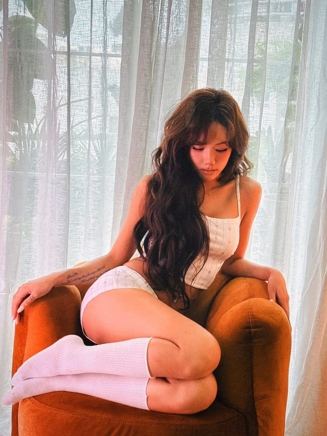 Giọng ca "Anh là ai" tạo dáng đa dạng trên chiếc ghế sofa màu vàng cam, từ ngả lưng đầy thư thái đến những khoảnh khắc trầm tư, bí ẩn, thậm chí là tinh nghịch ẩn mình sau chiếc ghế. (Ảnh: FBNV)