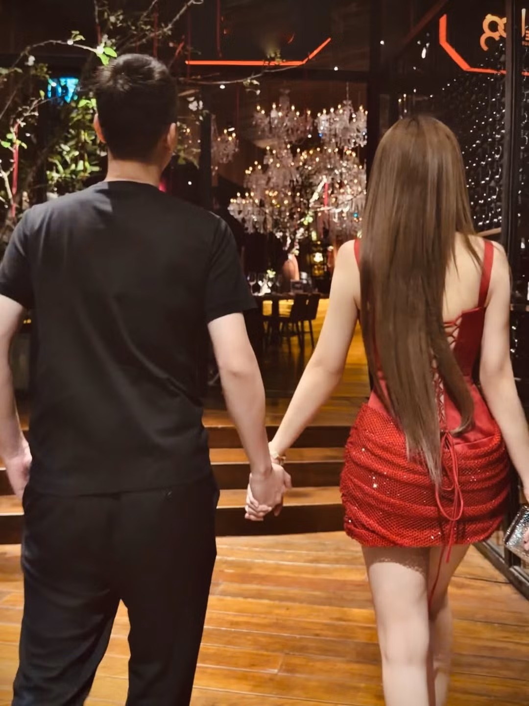 Trong những khung hình được chia sẻ, Huyền Baby không ngần ngại nắm chặt tay ông xã, cùng nhau bước vào không gian bữa tiệc được trang trí xa hoa với ánh đèn chùm rực rỡ và những kệ rượu vang đắt đỏ. (Ảnh: IGNV)