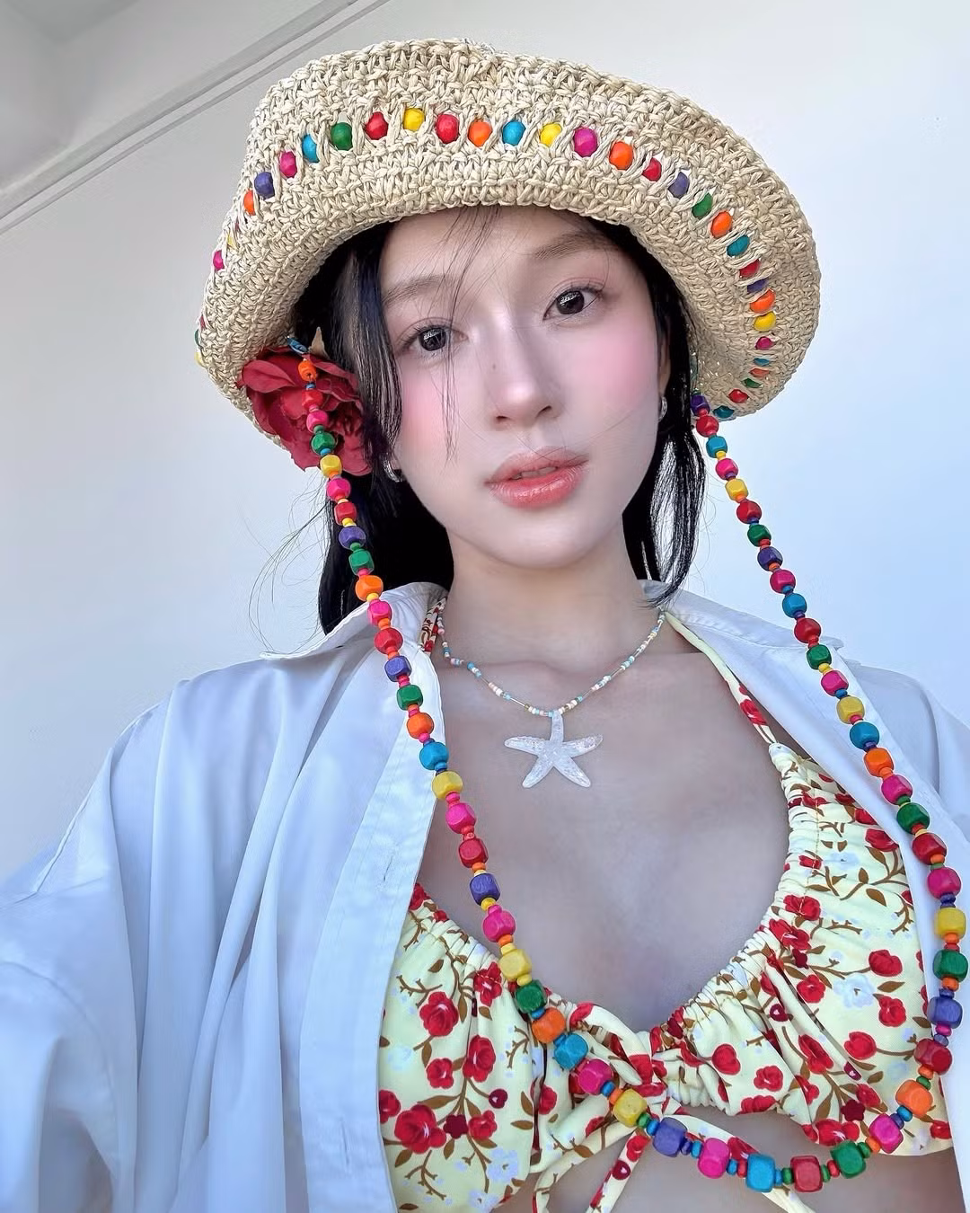 Điểm nhấn trong tạo hình là đóa hoa đỏ cài tóc – một chi tiết nhỏ nhưng giúp tổng thể trở nên mềm mại, nữ tính và đậm chất thơ giữa khung cảnh biển trời.