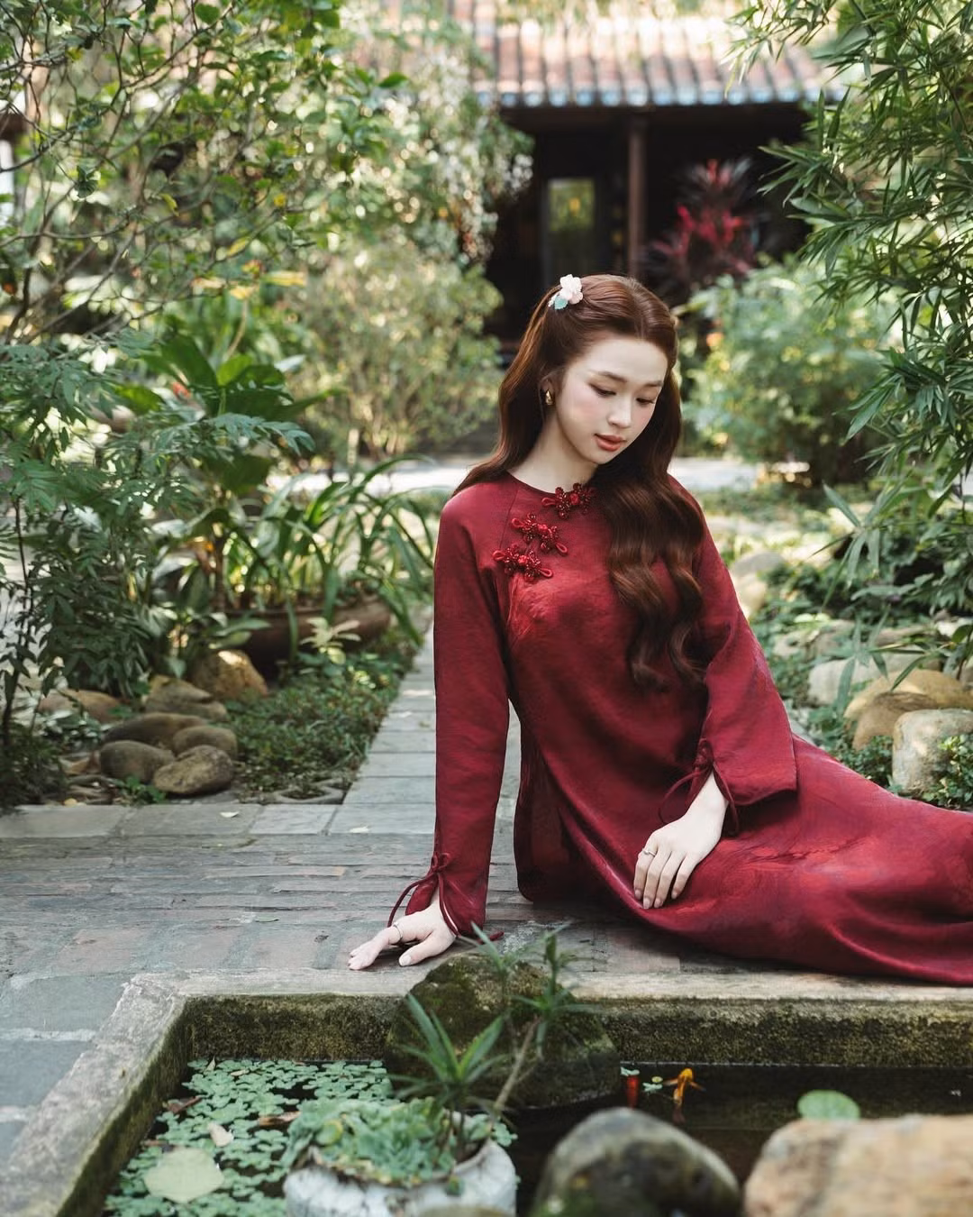 Thiết kế áo dài cổ tròn với hàng khuy tết thủ công mang đậm phong vị truyền thống. Sắc đỏ không chỉ tôn da mà còn mang ý nghĩa may mắn, giúp Karty Chang tỏa sáng rực rỡ giữa không gian xanh mướt của khu vườn. (Ảnh: IGNV)