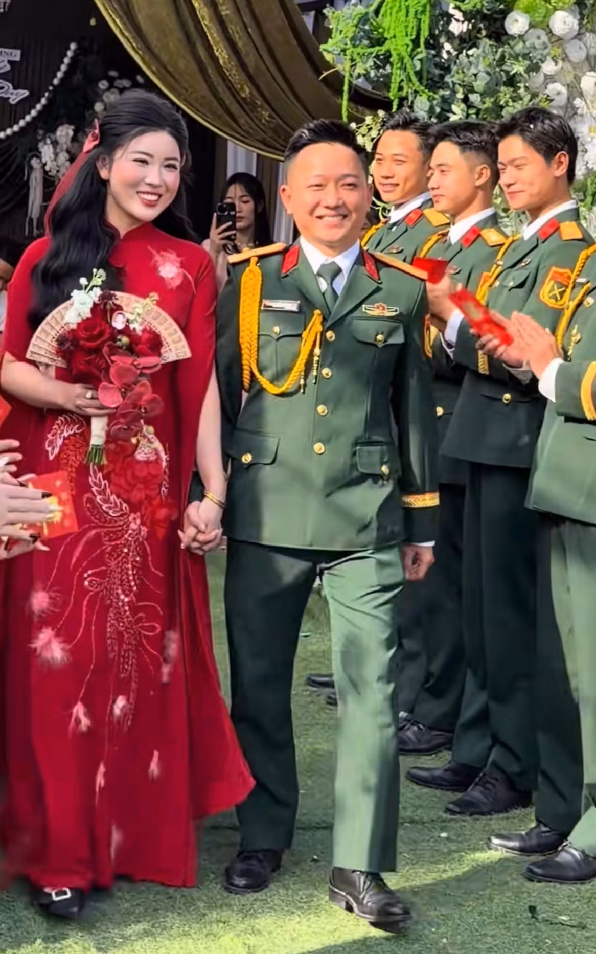 Chú rể cũng xuất hiện với trang phục quân phục, nắm tay cô dâu xinh đẹp trong tà áo dài đỏ thêu họa tiết rồng phượng cầu kỳ.