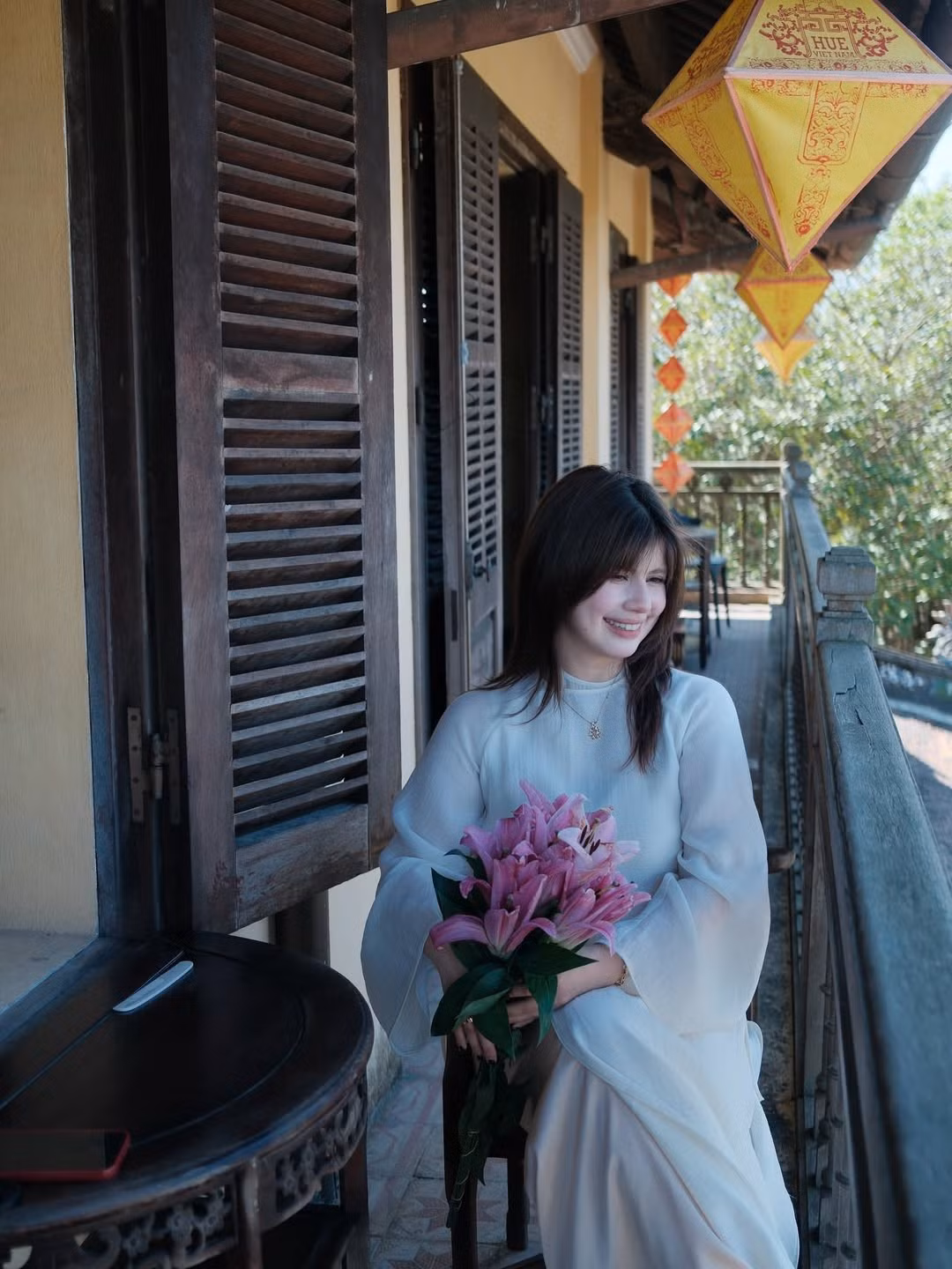 Địa điểm được Ebra Lê lựa chọn là một quán cafe giữa lòng Huế với kiến trúc cổ kính. Giữa bức tường rêu phong, những cánh cổng gỗ nhuốm màu thời gian, tà áo dài của Ebra như một gạch nối giữa quá khứ và hiện đại.(Ảnh: IGNV)
