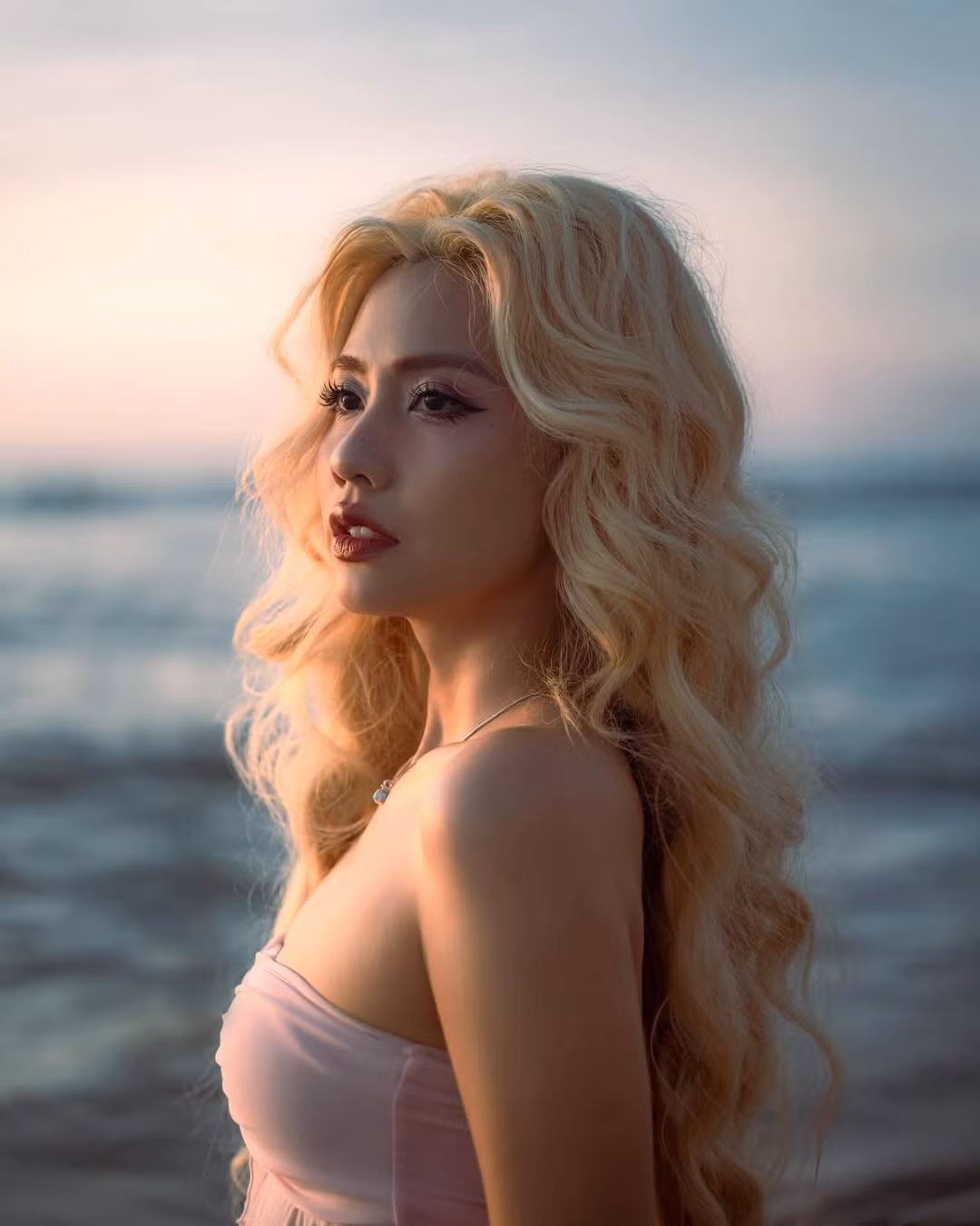 Cô nàng khoác lên mình bộ bikini màu hồng pastel dịu nhẹ, với phần áo quây xếp nhún bồng bềnh và quần cạp cao đồng điệu. Mái tóc bạch kim quen thuộc được uốn xoăn bồng bềnh, buông xõa tự nhiên, càng tôn lên vẻ đẹp mềm mại và nữ tính của cô.