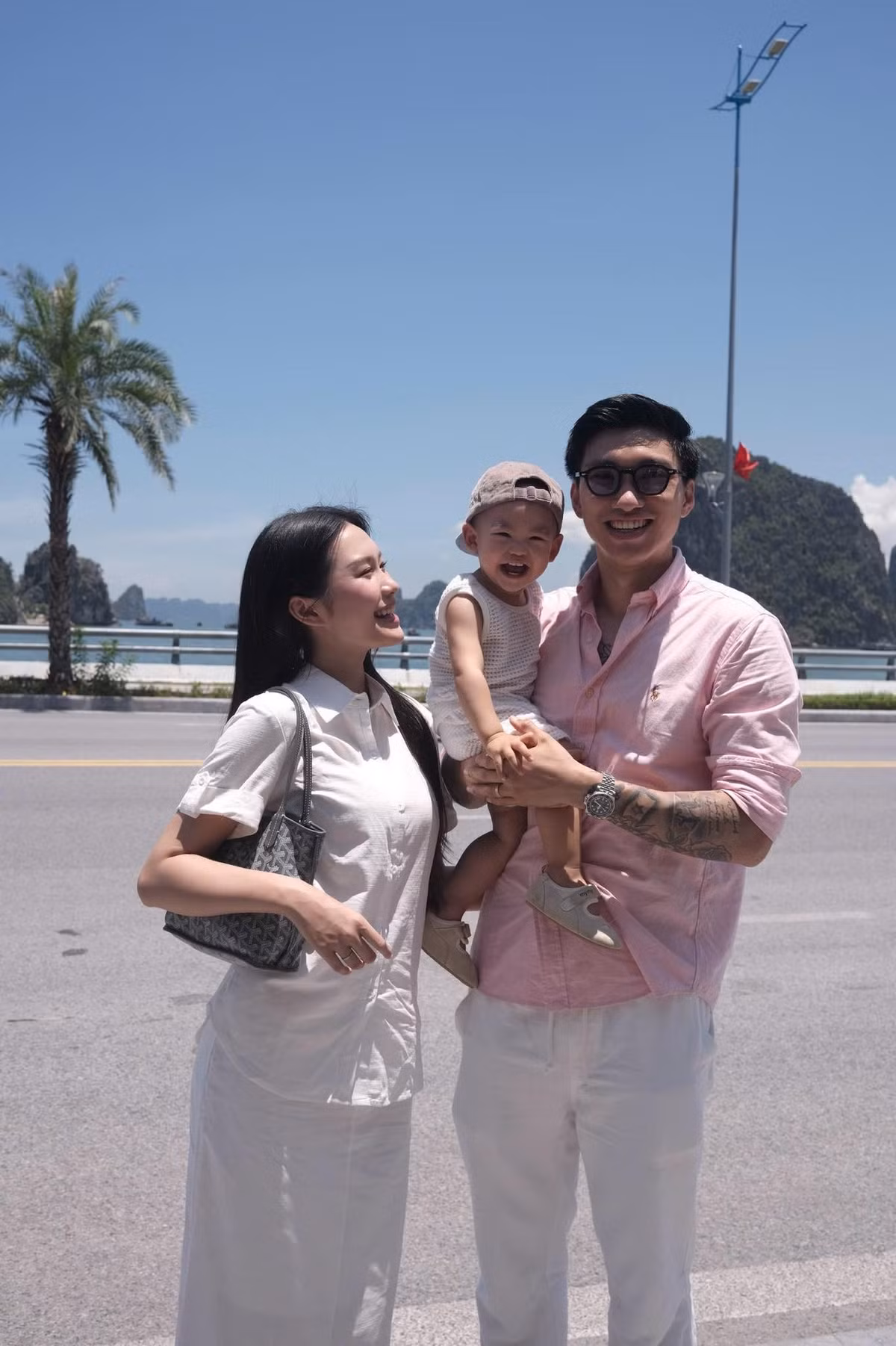 Cả hai đều chọn trang phục đơn giản, thoải mái. Cậu con trai nhỏ cũng diện trang phục tone trắng, được Đoàn Văn Hậu bế trên tay, cười tươi vui vẻ.