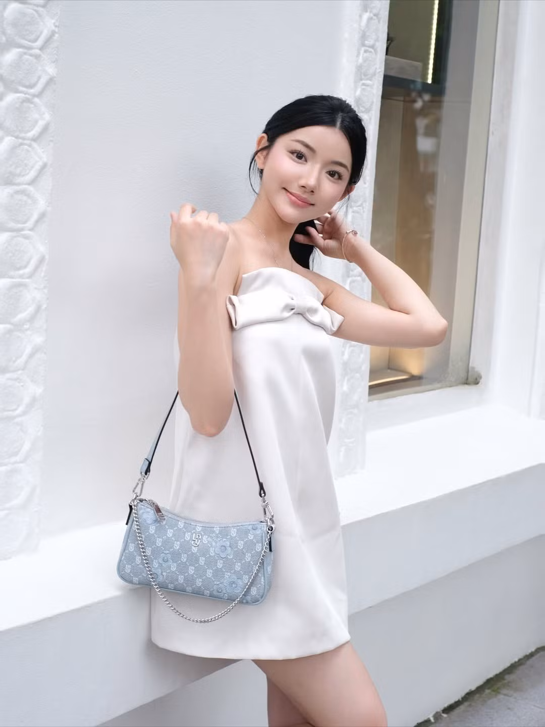 Chiếc túi xách kẹp nách màu xanh pastel với họa tiết monogram độc đáo và dây xích bạc trở thành điểm nhấn nhẹ nhàng, hài hòa với màu trắng của chiếc váy. (Ảnh: FBNV)