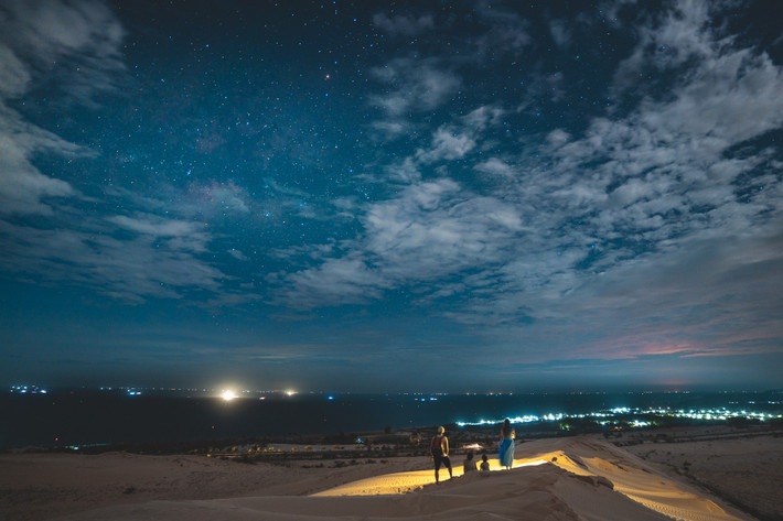 Nếu ban ngày, đồi cát Mũi Né (TP Phan Thiết, Bình Thuận) hấp dẫn bởi sắc vàng rực rỡ, từng con dốc mượt như lụa thu hút du khách trượt cát, thì về đêm, nơi này lặng lẽ đến lạ. Khi ánh nắng tắt dần sau lưng núi, cả không gian rộng lớn chìm vào màn tối, nhường chỗ cho ánh trăng vắt ngang bầu trời và gió nhẹ thổi lướt qua những rặng phi lao. Ảnh Nguyễn Hồng Nhật
