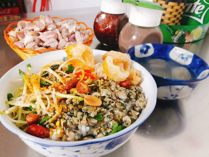 Nếu du khách đang muốn trải nghiệm vị dân dã đặc trưng của Huế, hãy ghé quán cơm hến Hoa Đông ở đường Ưng Bình. Chỉ với 10.000 – 20.000 đồng, bạn sẽ có một đĩa cơm hến đầy đủ hến xào, tóp mỡ giòn tan, rau sống thái nhỏ, đậu phộng và mắm ruốc cay – tất cả trộn đều với nước hến nóng, tạo nên hương vị cay nồng khó quên. Ảnh MIA