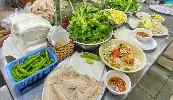 Ghé quán Bi Mỹ nằm trong khu ăn uống trong nhà, du khách không thể bỏ qua món bánh tráng cuốn thịt heo – một đặc sản gắn liền với ẩm thực Đà Nẵng. Một phần ăn đầy đặn gồm bánh tráng dai mềm, thịt heo thái lát mỏng, rổ rau sống tươi rói và đặc biệt là chén mắm nêm thơm nồng – yếu tố quyết định sự “gây nghiện” của món ăn. Mắm nêm ở đây không quá nặng mùi, pha sẵn với ớt xay cay cay, chấm miếng bánh tráng cuộn là đủ khiến thực khách xuýt xoa. Giá mỗi phần khoảng 40.000 – 50.000 đồng. Ảnh Foody