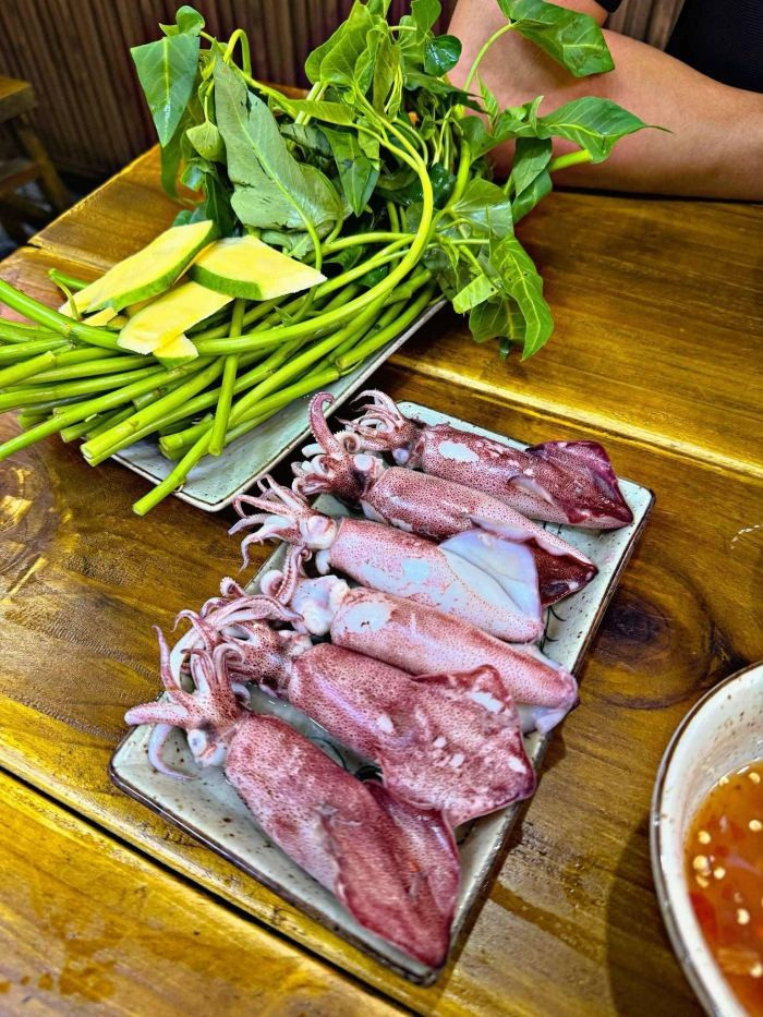 Sau khi bày mực hấp ra đĩa cùng rau muống sống và xoài xanh thái lát, món ăn đã sẵn sàng. Chỉ cần lấy bánh tráng, đặt rau muống, mực, xoài và hành lá vào, cuốn lại và chấm với nước mắm cay mặn là có thể thưởng thức. Món ăn hội tụ vị giòn ngọt của mực chín tới, vị thanh mát của rau và chút chua nhẹ từ xoài xanh. Nếu muốn no bụng hơn, có thể ăn kèm bún tươi. Ảnh Luhanhvietnam