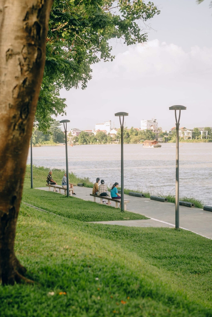 Địa điểm đang được yêu thích nằm ở đoạn ven sông giữa cầu Trường Tiền và cầu Mới – nơi có không gian mở, thoáng đãng và ánh sáng đẹp vào buổi chiều muộn. Thời gian lý tưởng để chụp ảnh là từ 16h30 đến 17h30, khi nắng dịu và màu trời trong xanh. Nên chọn góc chụp từ thảm cỏ hướng ra sông, lấy cầu Trường Tiền làm điểm nhấn phía sau. Để bức hình thêm phần nên thơ, du khách có thể mang theo phụ kiện như mũ rộng vành, váy trắng hoặc khăn voan nhẹ. Ảnh Dong Ho Vy