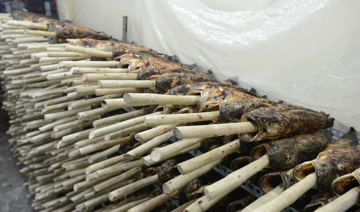 Những con cá đã được nướng sơ chất đầy trên kệ. Tất cả cá nướng đều được xiên bằng thân cây mía.