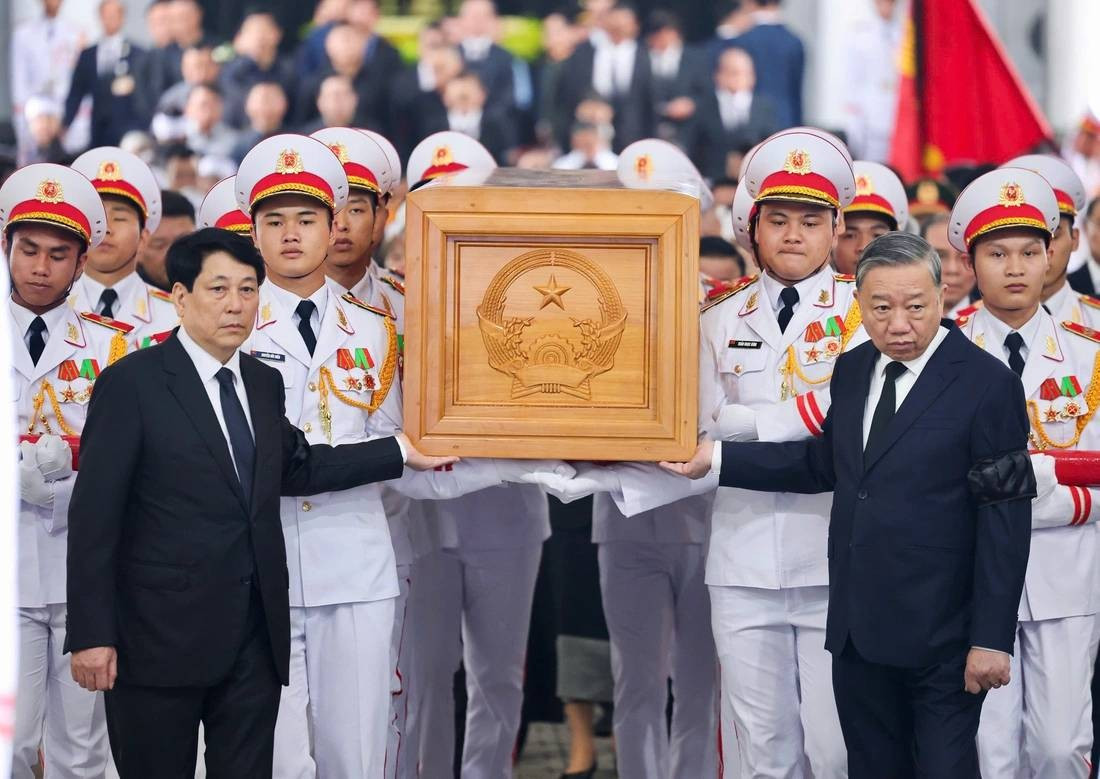 Tổng Bí thư Tô Lâm, Chủ tịch nước Lương Cường đặt tay lên linh cữu, đưa tiễn nguyên Chủ tịch nước Trần Đức Lương ra ngoài nhà tang lễ, tiến về phía linh xa. Phía sau là gia quyến, các đại biểu tiễn biệt nguyên Chủ tịch nước. (Ảnh Tuổi Trẻ)
