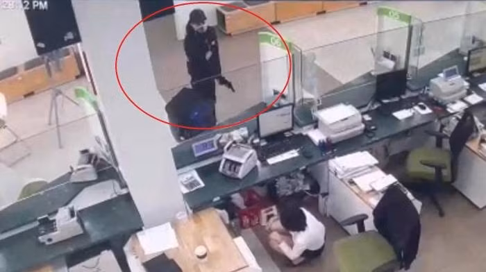 Thấy bảo vệ và nhân viên ngân hàng chưa có biểu hiện lo sợ, Nam lấy tiếp khẩu súng bút kéo chốt nổ một phát và yêu cầu nữ nhân viên ở quầy giao dịch phía trong để tiền lên bàn. Lúc này, nhân viên ngân hàng là chị N.T.H do hoảng sợ nên lấy 3.595.000.000 đồng trong các ngăn kéo tại quầy giao dịch để lên mặt bàn. Nam nhặt tiền cho đầy vào ba lô rồi kéo khóa đeo lên vai đi ra cửa. (Ảnh cắt từ clip)