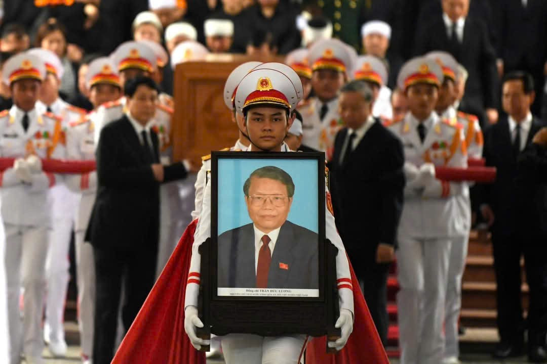 Bắt đầu lễ di quan, đưa linh cữu nguyên Chủ tịch nước Trần Đức Lương ra sân bay Nội Bài để về quê nhà Quảng Ngãi. Các sĩ quan QĐND Việt Nam và Đội nghi lễ chuẩn bị các thủ tục để tiến hành lễ di quan. Các sĩ quan QĐND Việt Nam rước di ảnh, khung gắn Huân chương, Huy chương của nguyên Chủ tịch nước. Phía sau, các chiến sĩ tiêu binh chia làm hai hàng khiêng linh cữu ra sân nhà tang lễ - nơi đặt cỗ linh xa.