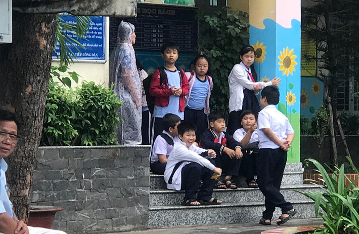 Nhiều em học sinh tiểu học chờ người thân đến đón về vào trưa ngày 25/12 giữa lúc trời đã bắt đầu mưa to, gió lớn.