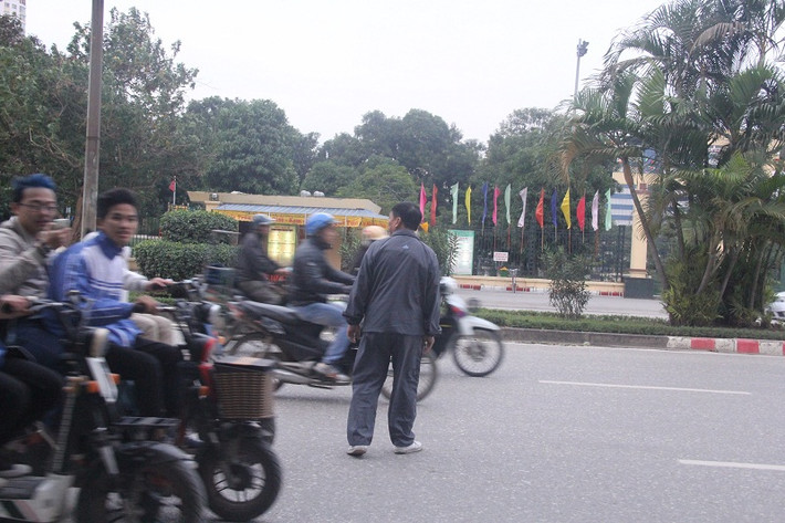 Một người lớn tuổi băng qua các đầu xe máy bất chấp nguy hiểm.