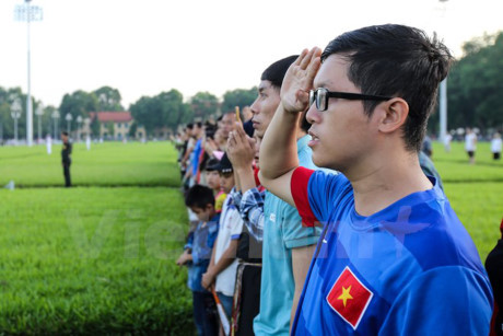 Mọi người dân từ già đến trẻ đều nghiêm trang hướng về cột cờ. (Ảnh: Minh Sơn/Vietnam+)