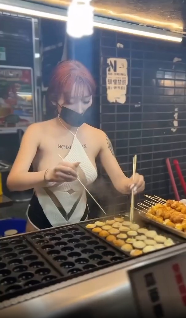 Cô gái bán hàng này mặc một chiếc quần cực ngắn ôm sát, áo yếm gợi cảm, để lộ phần lớn cơ thể. Trang phục này hoàn toàn khác biệt so với những người bán hàng khác, vốn thường chọn những bộ đồ kín đáo, thoải mái để tiện lợi cho công việc.