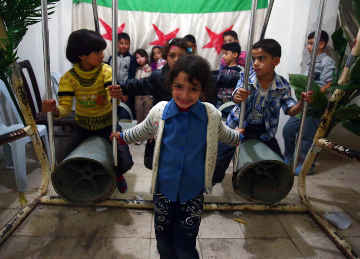 Nụ cười rạng rỡ của bé gái Syria bên chiếc xích đu bằng vỏ đạn tên lửa của trẻ em đất nước Trung Đông đang bị chiến tranh tàn phá.
