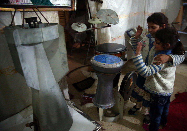 2 bé gái Syria đứng trước dàn nhạc với các nhạc cụ được chế tạo từ các loại vũ khí...