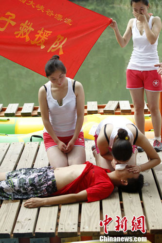 Một cô gái trẻ thực hành hô hấp nhân tạo và xoa bóp tim ngoài lồng ngực khẩn cấp trên một người đàn ông thực sự. Đằng sau, một cô gái trẻ khác tỏ ra ái ngại.