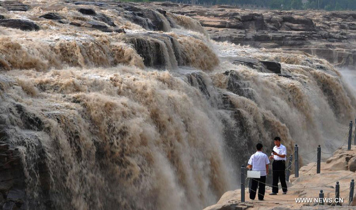 Hai khách du lịch đứng trước dòng chảy dữ dội của nước lũ khi tràn qua thác Hukou trên sông Hoàng Hà.