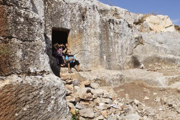 Một nhóm trẻ em Syria ngồi chơi bên ngoài cửa động ở núi Al-Arbaeen ở Idlib sau khi các gia đình di cư xuống lòng đất để tránh chiến tranh.