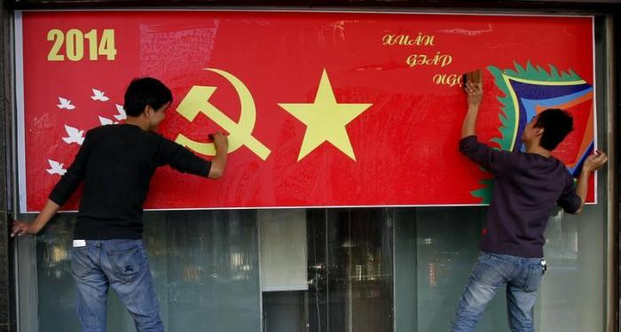 Hai thanh niên Việt Nam treo tấm áp phích lớn trên một đường phố ở Hà Nội, chào mừng năm mới (âm lịch) ngày 23/1. Ảnh: Reuters.