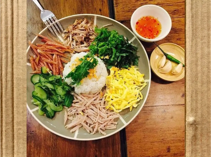 Cơm âm phủ Huế là một trong những món ăn đặc sản mang đậm nét văn hóa Huế. Món ăn được chế biến từ nhiều nguyên liệu, cơm trắng thường đặt ở giữa, xung quanh là rau xanh, cải chua, thịt ba rọi, nem chua, chả Huế,... và được trang trí bằng một ít hành, ngò. Ảnh: Traveloka