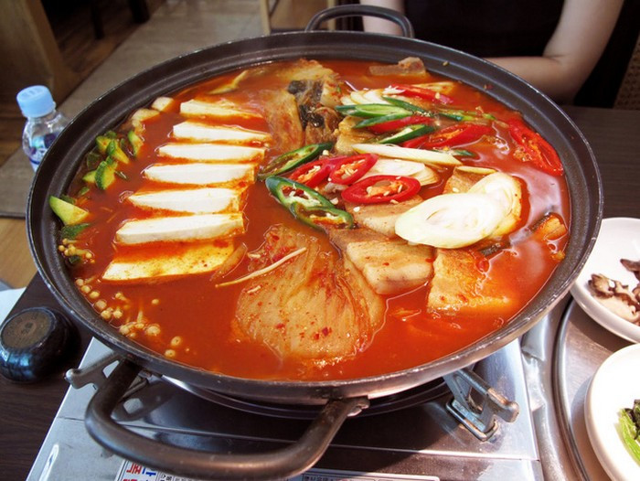 Thái kim chi thành khúc vừa ăn, đậu phụ thái miếng, hành tím băm nhuyễn, hành lá rửa sạch thái nhỏ. Phi thơm hành tím băm rồi cho thịt vào xào chín thì thả kim chi vào, đảo đều tay để kim chi ngấm dầu rồi đổ nước vào, xăm xắp mặt và tiếp tục đun. Nấu đến khi canh sôi chừng vài phút thì cho đậu non vào, đảo nhẹ tay để đậu không nát. Cuối cùng là thả hành lá vào rồi tắt bếp. Ảnh: Enbac.
