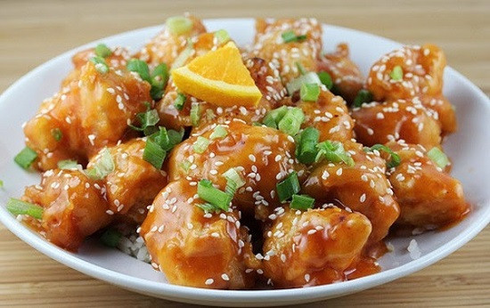 Vẫn dùng chảo rán gà, đổ bớt lượng dầu thừa. Phi nửa phần vỏ cam đã bào và tỏi, sau đó đổ nước cam, chế thêm nước mắm. Đợi đến khi hỗn hợp sôi lên thì cho gà vào, để lửa nhỏ, om đến khi nước đặc sệt lại là được. Đổ gà ra đĩa. Cho hành lá và chút vừng trắng lên để trang trí. Ảnh: toinayangi.vn.