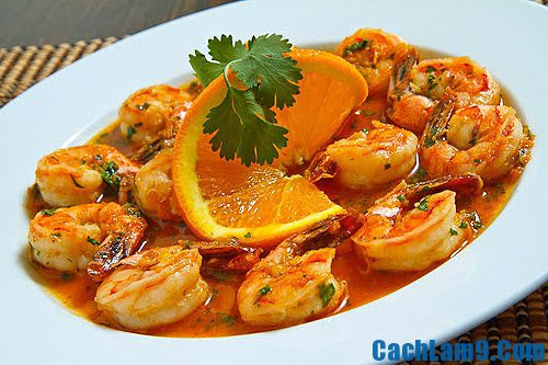 Liên tục đảo đều tay để tôm ngấm gia vị đến khi nước xốt sền sệt bao quanh tôm rất hấp dẫn, cho hành lá thái mịn, ớt thái lát vào đảo thêm vài lần nữa. Cho món tôm sốt cam ra đĩa đã trang trí những lát cam thái mỏng, dàn đều, rắc ngò rí và một ít tiêu lên trên. Ảnh: cachlam9.com.